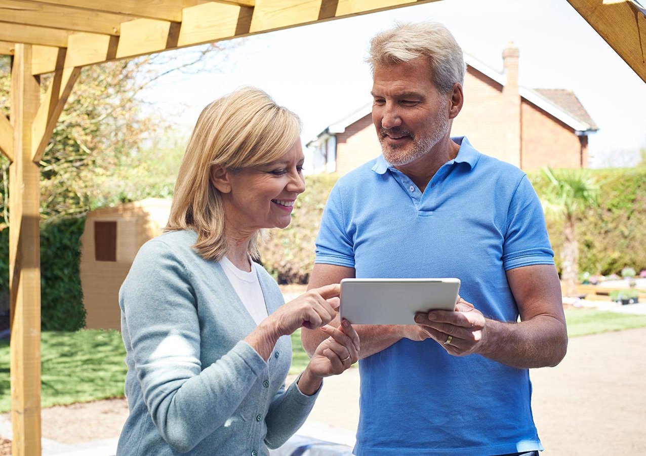 Ein Mann und eine Frau stehen unter einer Terrassenüberdachung mit einem Tablet in der Hand